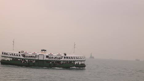 Eine-Fähre-Fährt-An-Einem-Nebligen-Tag-Im-Hafen-Von-Hongkong-Mit-Entfernten-Booten-Und-Einer-Schwachen-Skyline