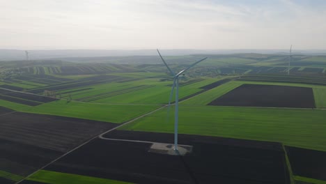 Wind-turbine-stands-tall-in-vast-green-and-black-patchwork-fields-on-a-foggy-day