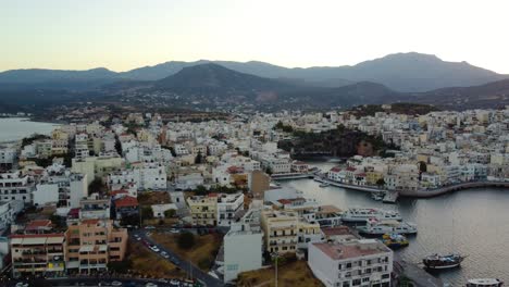 Vista-Panorámica-Aérea-Orbital-Izquierda-De-La-Ciudad-Costera-De-Agios-Nikolaos-Y-El-Lago-Voulisméni,-Creta,-Grecia