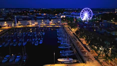 Approaching-aerial-movement-to-the-Vieux-Port-with-Grande-roue-at-night,-La-Rochelle,-France