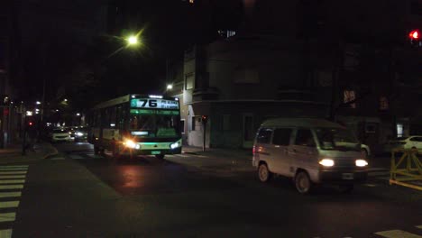 Wide-shot-of-a-76-autobus-driving-streets,-commuter-public-transport-of-Buenos-aires-city-at-night,-argentine-neighborhood-traffic