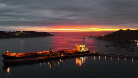 Cloudy-sunset-with-red-rays-over-a-cargo-ship-stopped-at-La-Herradura-beach,-Coquimbo,-Chile