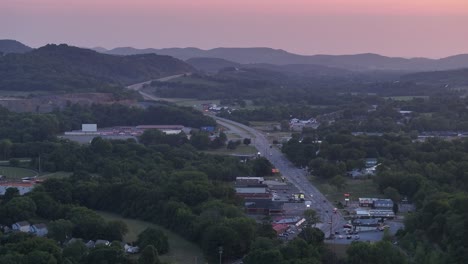 Luftaufnahme-Einer-Autobahn,-Die-Bei-Sonnenuntergang-Durch-Eine-Kleinstadt-Im-Ländlichen-Amerika-Führt