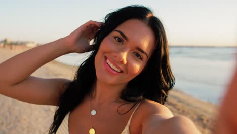 Woman-Taking-Selfie-and-Blowing-Kiss-on-Beach.people,-summer-and-swimwear-concept-happy-smiling-young-woman-in-bikini-swimsuit-taking-selfie-and-blowing-kiss-on-beach