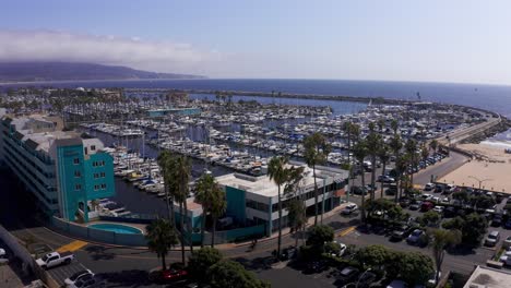 Low-reverse-pullback-aerial-shot-of-King-Harbor-Marina-looking-towards-the-Palos-Verdes-peninsula-in-Redondo-Beach,-California