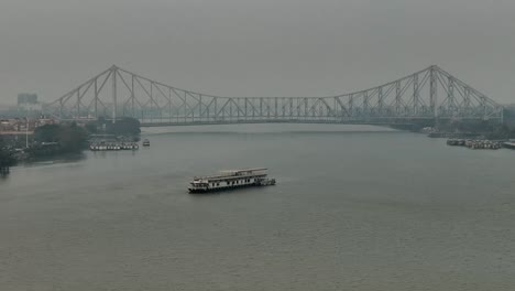 Aerial-shot-of-Howrah-Bridge-Kolkata-West-Bengal-India-with-a-white-tourist-boat-in-the-river-Hooghly