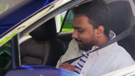 Smiling-Indian-Man-or-Driver-Driving-Car.transport,-safety-and-people-concept-happy-smiling-indian-man-or-driver-fastening-seat-belt-in-car