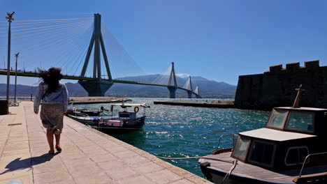 Mujer-Caminando-Por-El-Golfo-De-Corinto,-Grecia,-Junto-Al-Puente-Rio-Antirio