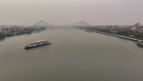 Aerial-shot-of-Howrah-Bridge-in-Kolkata-with-a-big-white-tourist-boat-in-the-middle-of-the-Hooghly-river