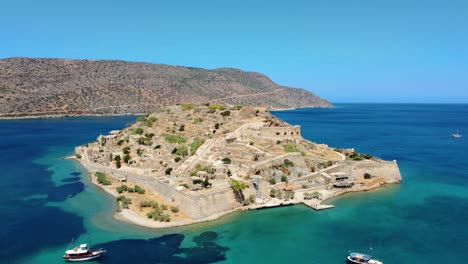 Orbit-Blick-über-Die-Festungsinsel-Spinalonga-Und-Einige-Fischerboote-Auf-Türkisfarbenem-Wasser,-Griechenland