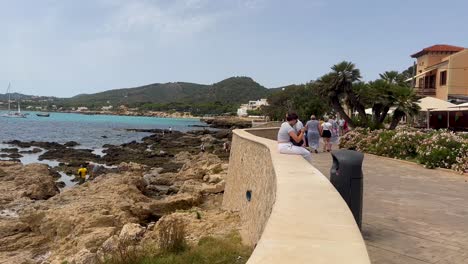 People-enjoying-a-sunny-day-on-a-rocky-beachside-promenade-in-Mallorca,-Spain