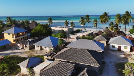 Dolly-in-flight-over-Pingwe-Village-reveal-turquoise-waters-and-anchored-boats,-Zanzibar