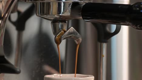 Espresso-making-process,-coffee-pouring-from-portafilter-of-coffee-machine-into-espresso-cup