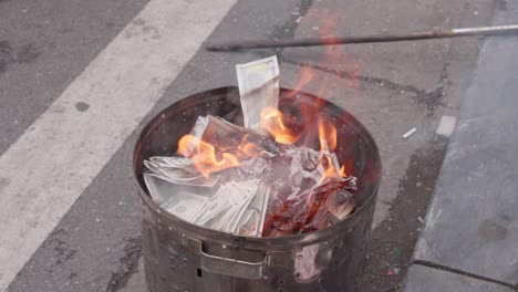 Close-up-view,-hand-throw-paper-fake-money-on-fire-in-metal-bucket,-slow-motion