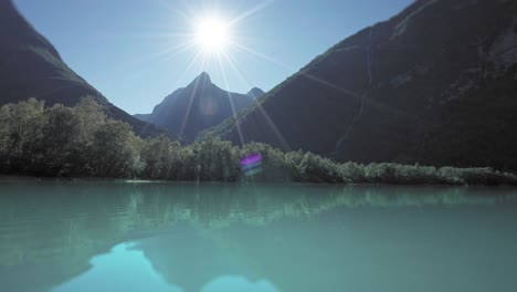 Vista-Panorámica-De-Un-Lago-Tranquilo-Con-Frondosos-árboles-Y-Montañas,-Iluminado-Por-El-Sol-De-La-Mañana.