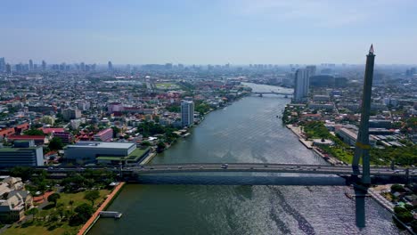 Bangkok,-Thailand,-Southeast-Asia---The-Iconic-Rama-VIII-Bridge-Spans-the-Chao-Phraya-River,-With-the-Civic-Landscape-as-its-Backdrop---Aerial-Pullback-Shot