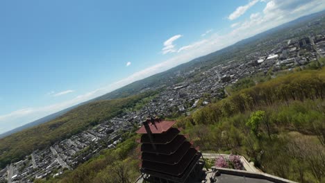 Bandera-Estadounidense-Ondeando-En-La-Cima-De-Una-Montaña-Con-Un-Edificio-De-Pagoda-Y-El-Paisaje-Urbano-De-Redding-Al-Fondo