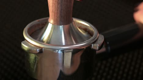 Tamping-freshly-grounded-coffee-beans,-close-up-of-tamper-in-process