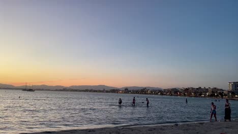 People-enjoying-the-calm-waters-at-sunset-on-a-beach-in-Mallorca,-Spain