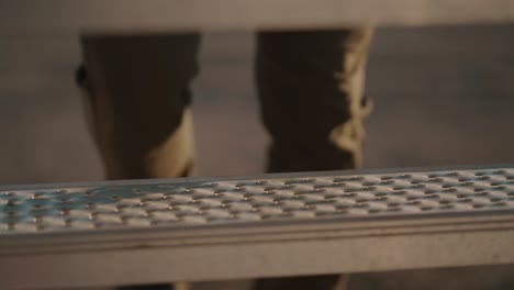 Worker-climbing-metallic-stairs-at-a-construction-site-during-sunset,-close-up,-outdoor-shot