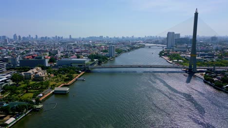 Bangkok,-Tailandia,-Sudeste-Asiático:-Una-Vista-Impresionante-Del-Puente-Rama-VIII-Que-Se-Extiende-Sobre-El-Río-Chao-Phraya,-Con-El-Paisaje-Urbano-Como-Telón-De-Fondo:-Toma-Aérea