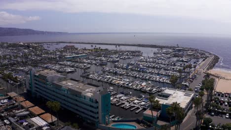 Aerial-low-panning-shot-of-the-King-Harbor-Marina-with-the-Palos-Verdes-peninsula-in-the-distance-in-Redondo-Beach,-California