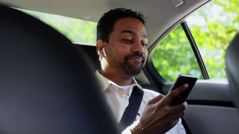 Pasajero-Con-Auriculares-Y-Teléfono-Móvil-En-Un-Taxi.-Concepto-De-Transporte,-Negocios-Y-Tecnología.-Pasajero-Indio-Sonriente-Feliz-Con-Auriculares-Inalámbricos-Usando-Un-Teléfono-Inteligente-En-El-Asiento-Trasero-De-Un-Taxi.