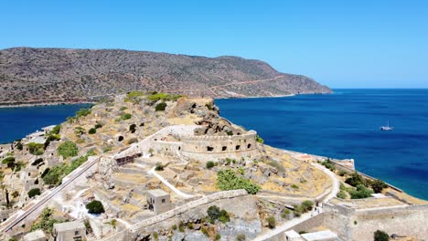 Revealing-Aerial-Moving-Away-of-Spinalonga-Island-Venetian-Fortress-Bastion,-Crete,-Greece