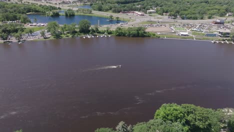 Vista-Aérea-Panorámica-De-Un-Kayakista-Remando-En-El-Río-Mississippi-Durante-El-Día-Con-Una-Ciudad-Al-Fondo-En-Minnesota,-EE.-UU.