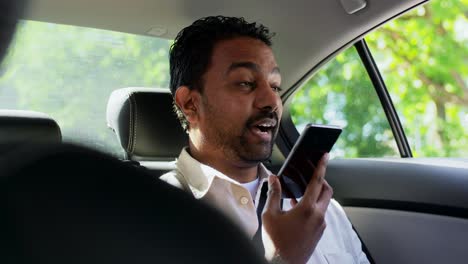 Male-Passenger-Calling-on-Smartphone-in-Taxi-Car.transport,-business-and-technology-concept-happy-smiling-indian-male-passenger-or-businessman-using-voice-command-recorder-on-smartphone-on-back-seat-of-taxi-car