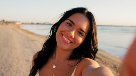 Woman-Taking-Selfie-and-Blowing-Kiss-on-Beach.people,-summer-and-swimwear-concept-happy-smiling-young-woman-in-bikini-swimsuit-taking-selfie-and-blowing-kiss-on-beach