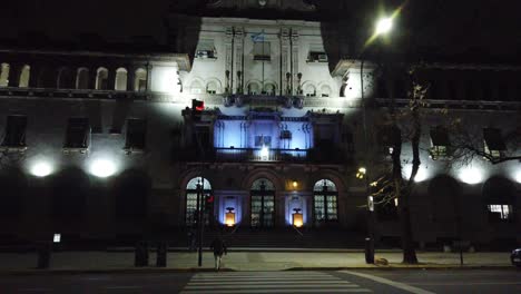 Los-Peatones-Cruzan-Las-Calles-De-La-Avenida-Gaona,-El-Hospital-Policlínico-Del-Barrio-Caballito,-Lugar-Emblemático-Y-Sus-Luces-De-Neón-Iluminadas-Por-La-Noche.