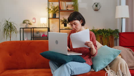 Exhausted-woman-freelancer-with-paperwork-using-laptop-computer-throwing-documents-in-air-at-home