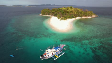 4K-drone-video-of-a-group-of-people-all-jumping-off-a-sailing-boat-into-crystal-clear-turquoise-water-near-a-tropical-island-in-Palawan,-Philippines