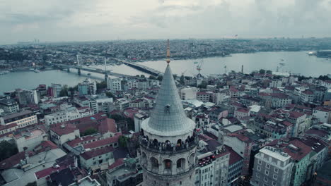 Close-view-on-the-Galata-Tower-on-a-cloudy-grey-day-in-Istanbul,-Turkey,-river-in-the-background,-slow-motion,-pan-shot-around-tower