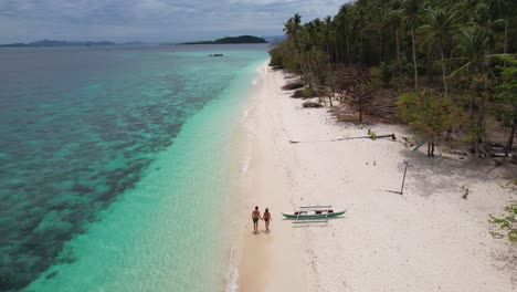 4K-drone-video-of-a-couple-walking-hand-in-hand-along-a-white-sand-beach-on-a-tropical-island-in-Palawan,-Philippines