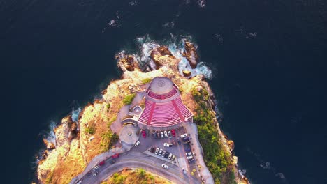 Top-down-scenic-aerial-with-cars-passing-by-the-iconic-and-colorful-Symphony-of-the-Sea-Amphitheater-in-Acapulco,-Mexico