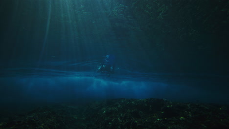 Pan-across-reef-to-surfer-duck-diving-to-escape-powerful-wave-as-light-rays-shine-and-textured-vortex-of-wave-grows