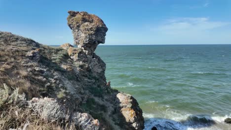 A-stunning-natural-rock-formation-stands-at-the-edge-of-the-Sea-of-Azov,-resembling-a-human-head-amidst-vibrant-coastal-scenery-in-Crimea