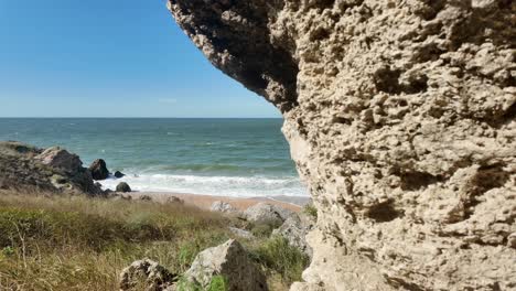 Waves-gently-crash-against-the-sandy-shore,-framed-by-rugged-rocks-and-lush-vegetation-on-a-clear-day-in-Crimea’s-beautiful-coastline