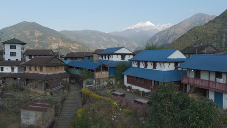 Drone-shot-of-aesthetic-village-of-Lamjung,-Nepal,-surrounded-by-mountains,-hills,-greenery,-and-traditional-housing