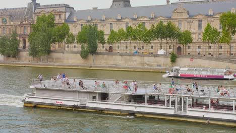 Riverboats-on-the-Seine-during-the-Olympic-Games-in-Paris,-the-Louvre-Museum-in-the-background