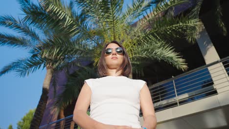 Woman-with-sunglasses-stand-under-palm-tree-and-point-finger,-Mallorca