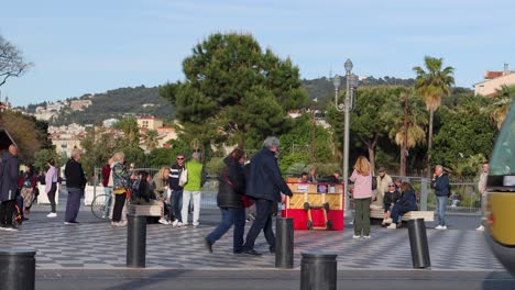 People-walk-past-tram-at-Place-Massena-in-Nice,-France,-focus-on-motion-and-urban-setting