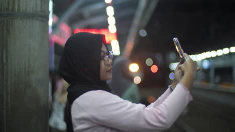 Indonesische-Muslimin-Macht-Ein-Selfie-Mit-Ihrem-Handy,-Während-Sie-Am-Elektrischen-Bahnhof-Kampung-Bandan-In-Jakarta-Auf-Den-Zug-Wartet