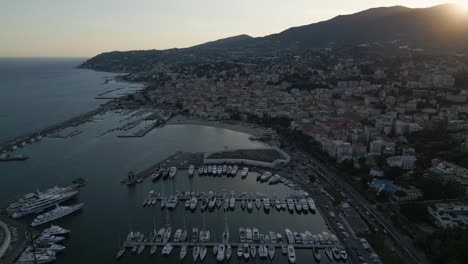 Vista-Aérea-Del-Atardecer-Desde-San-Remo,-Italia,-Riviera,-Costa,-Drones,-Gli,-Sobre-La-Playa-Y-El-Puerto,-Con-La-Ciudad-En-La-Colina