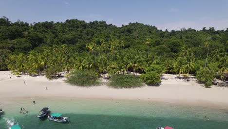 Vista-Aérea-De-Una-Prístina-Playa-Tropical-En-Panamá-Con-Aguas-Turquesas-Cristalinas,-Exuberante-Vegetación,-Palmeras-Y-Varios-Barcos-Anclados-A-Lo-Largo-De-La-Costa.