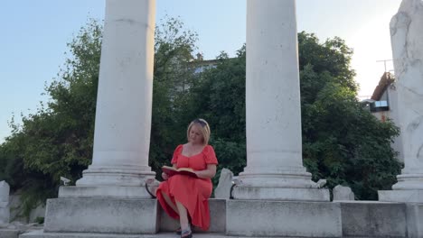 Woman-in-orange-dress-reads-a-book-and-contemplates-between-the-columns-of-the-Roman-Forum-of-Philippopolis