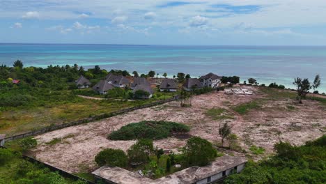 Dolly-in-aerial-of-beachfront-rustic-bungalows-and-blue-turquoise-waters-lagoon-in-Zanzibar,-Tanzania