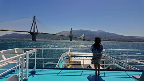 Attractive,-young-woman-on-a-ferry-with-a-view-of-the-Rio–Antirrio-Bridge-or-Charilaos-Trikoupis-Bridge,-Greece